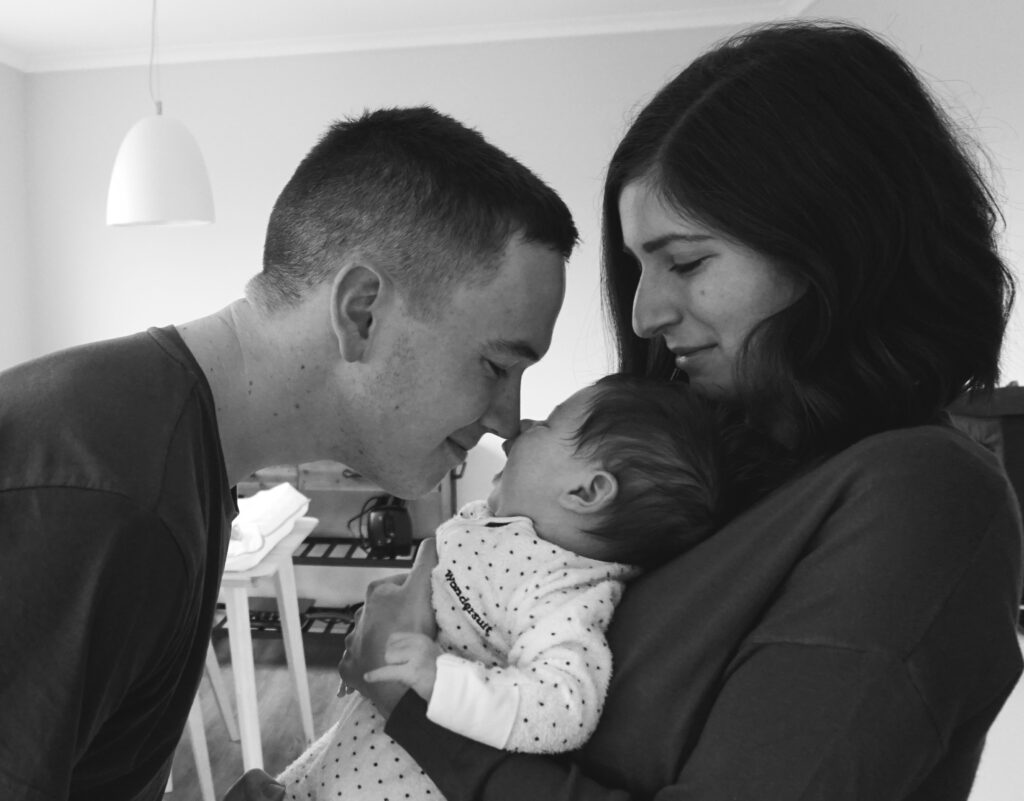 A mother and father holding their baby and smiling