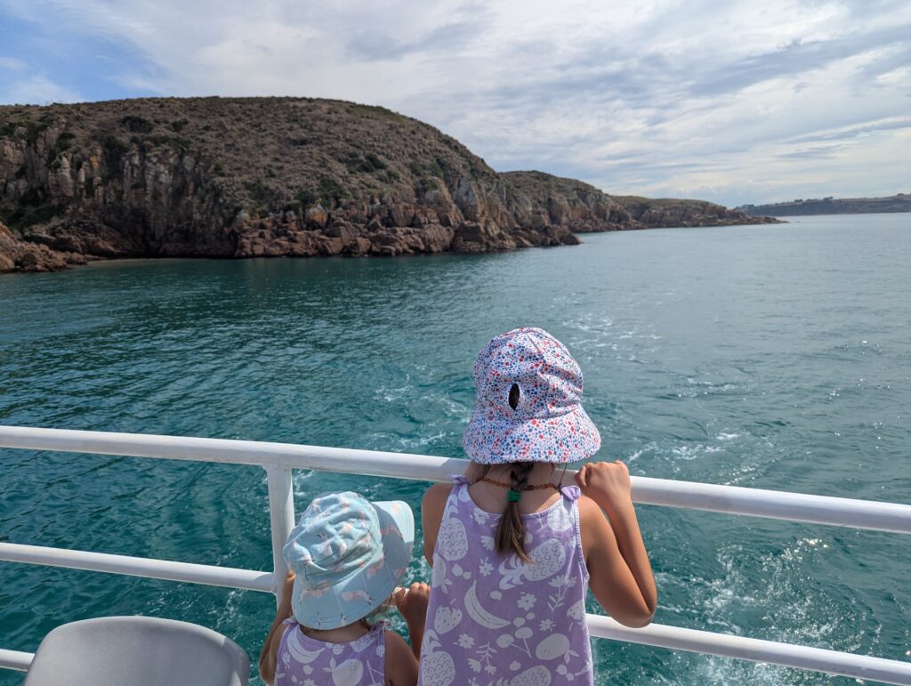 Two kids on a boat overlooking the ocean and rocky cliffs