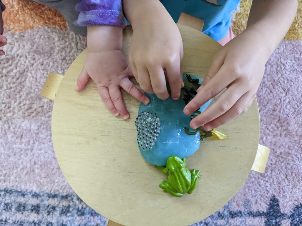 Kids hands playing with toy frogs and play dough pond